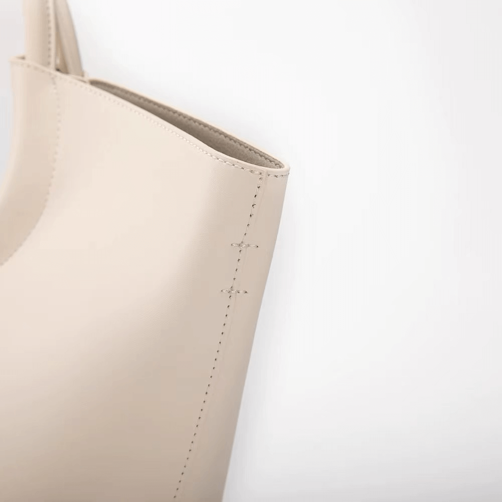 Close-up of a beige leather bag with visible stitching on a light gray background