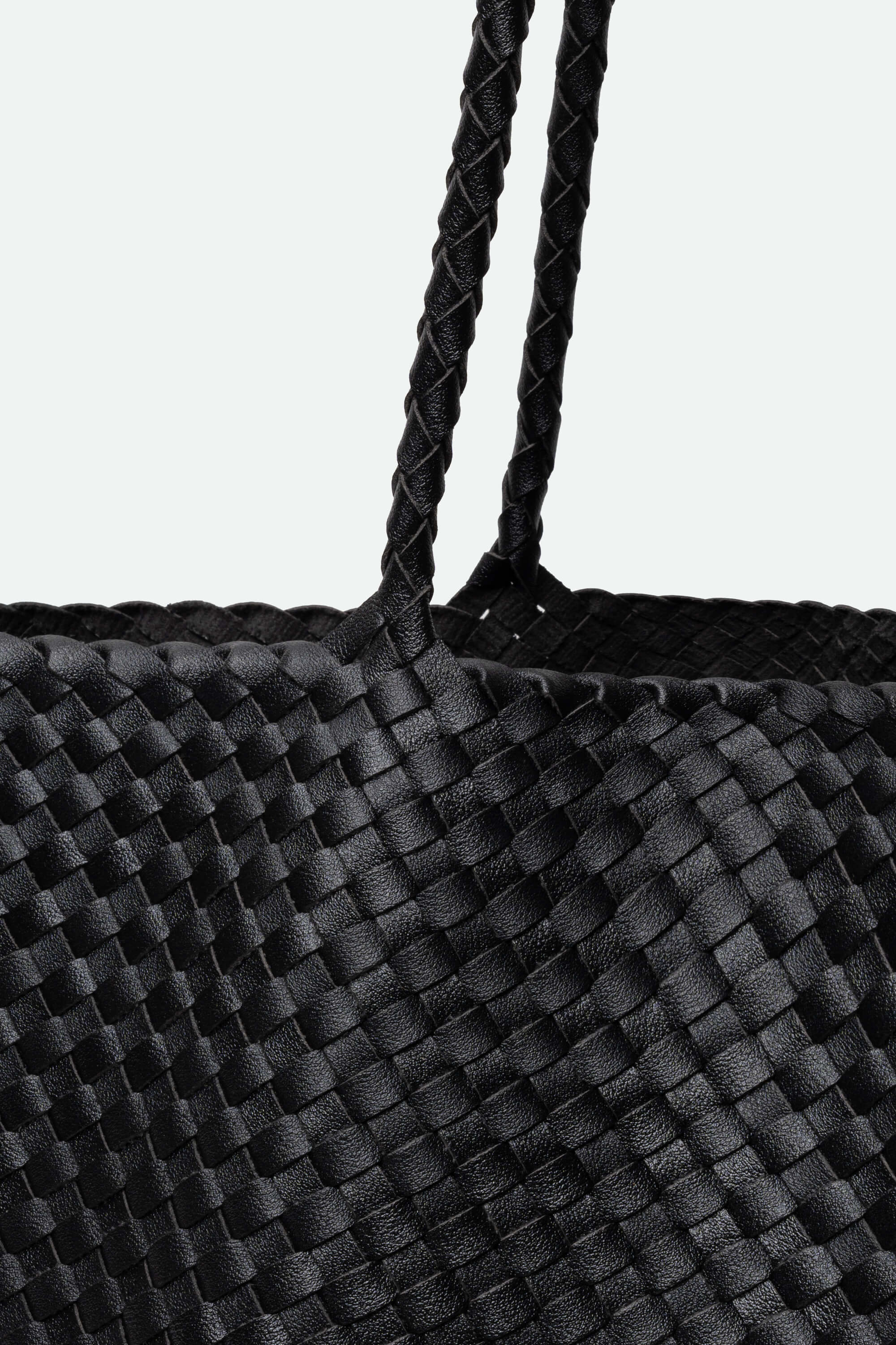 Close-up of a black woven bag with braided handle on a light gray background