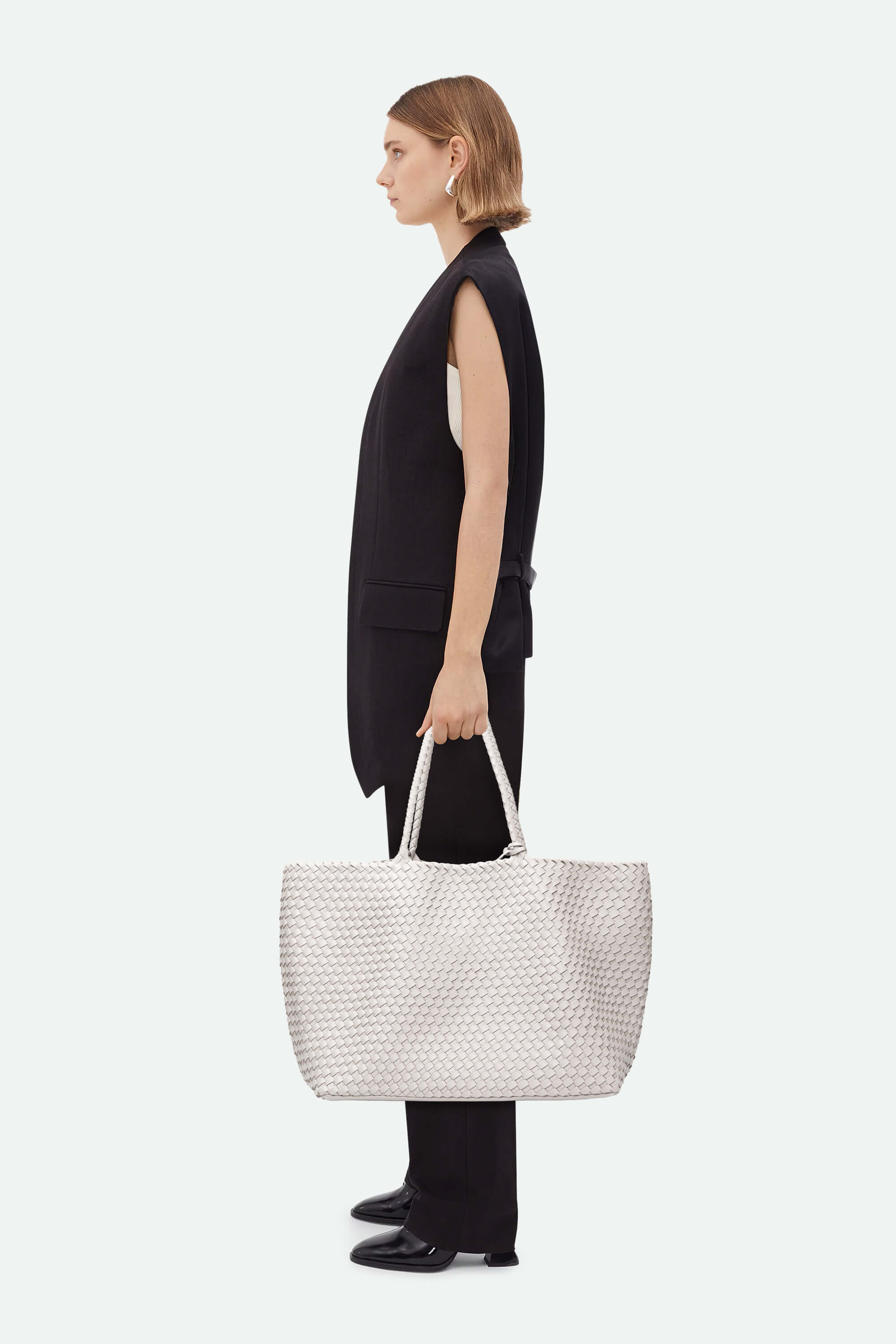 Woman holding a white woven handbag against a white background