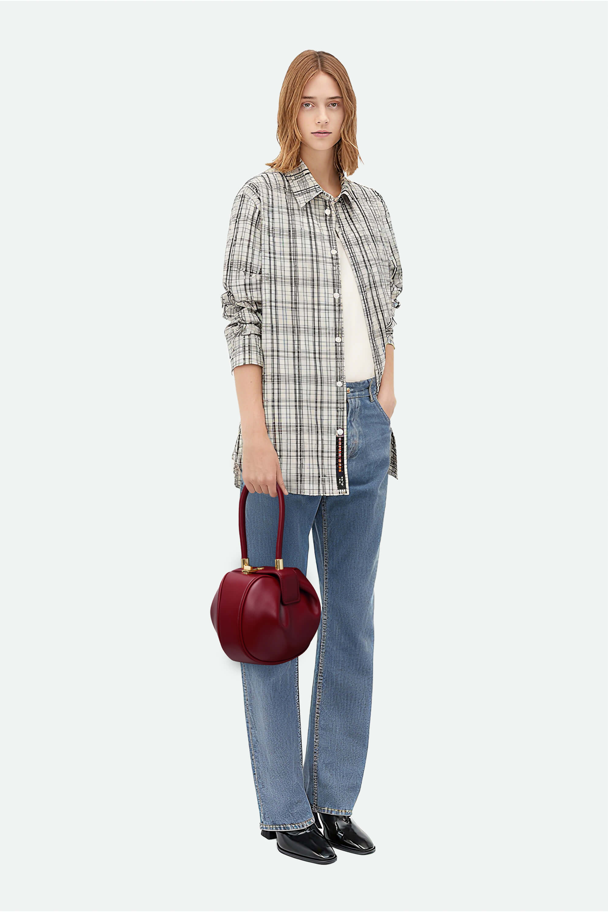 Woman holding a red handbag wearing a plaid shirt, jeans, and black shoes on a white background