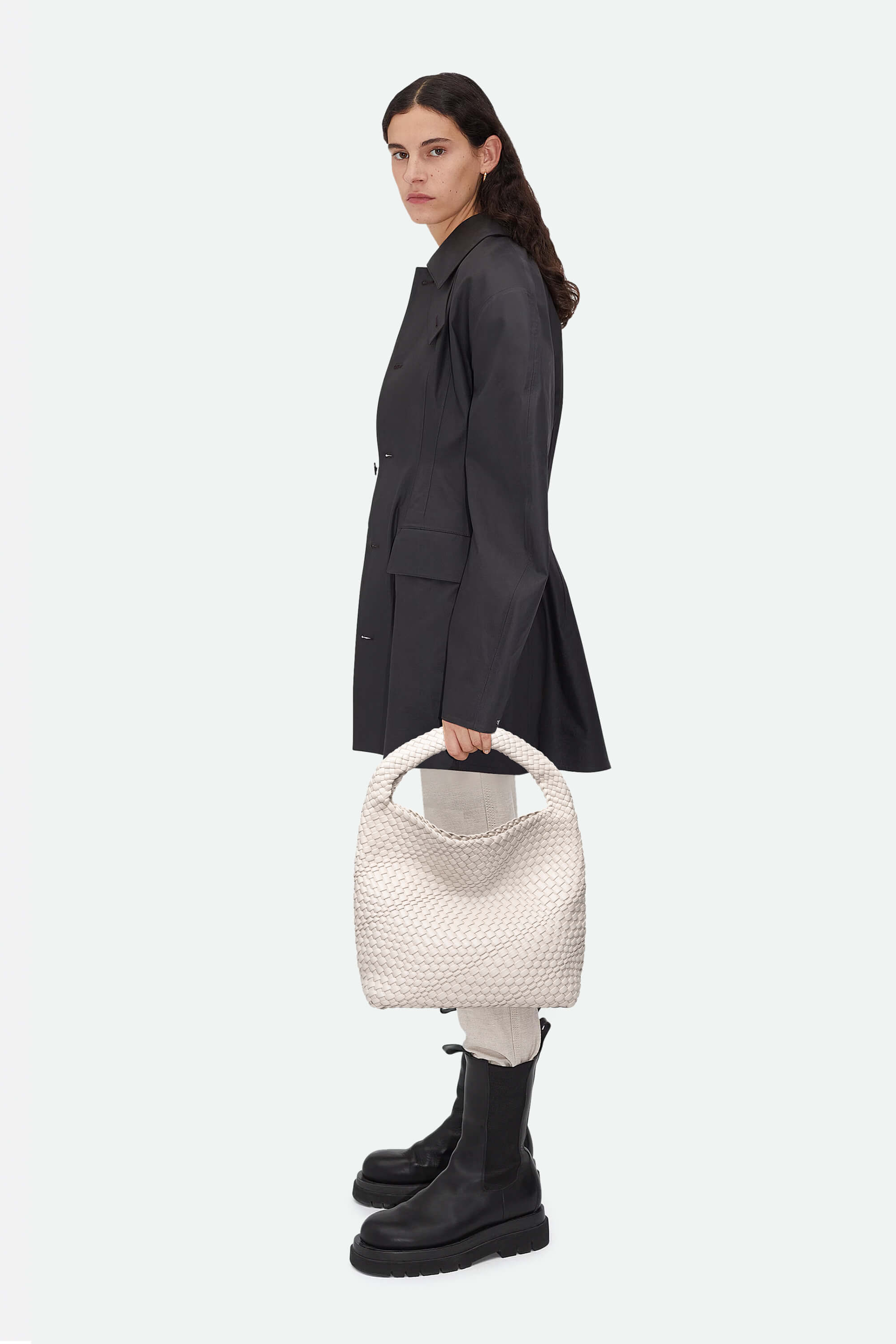 Woman holding a white textured handbag against a plain background