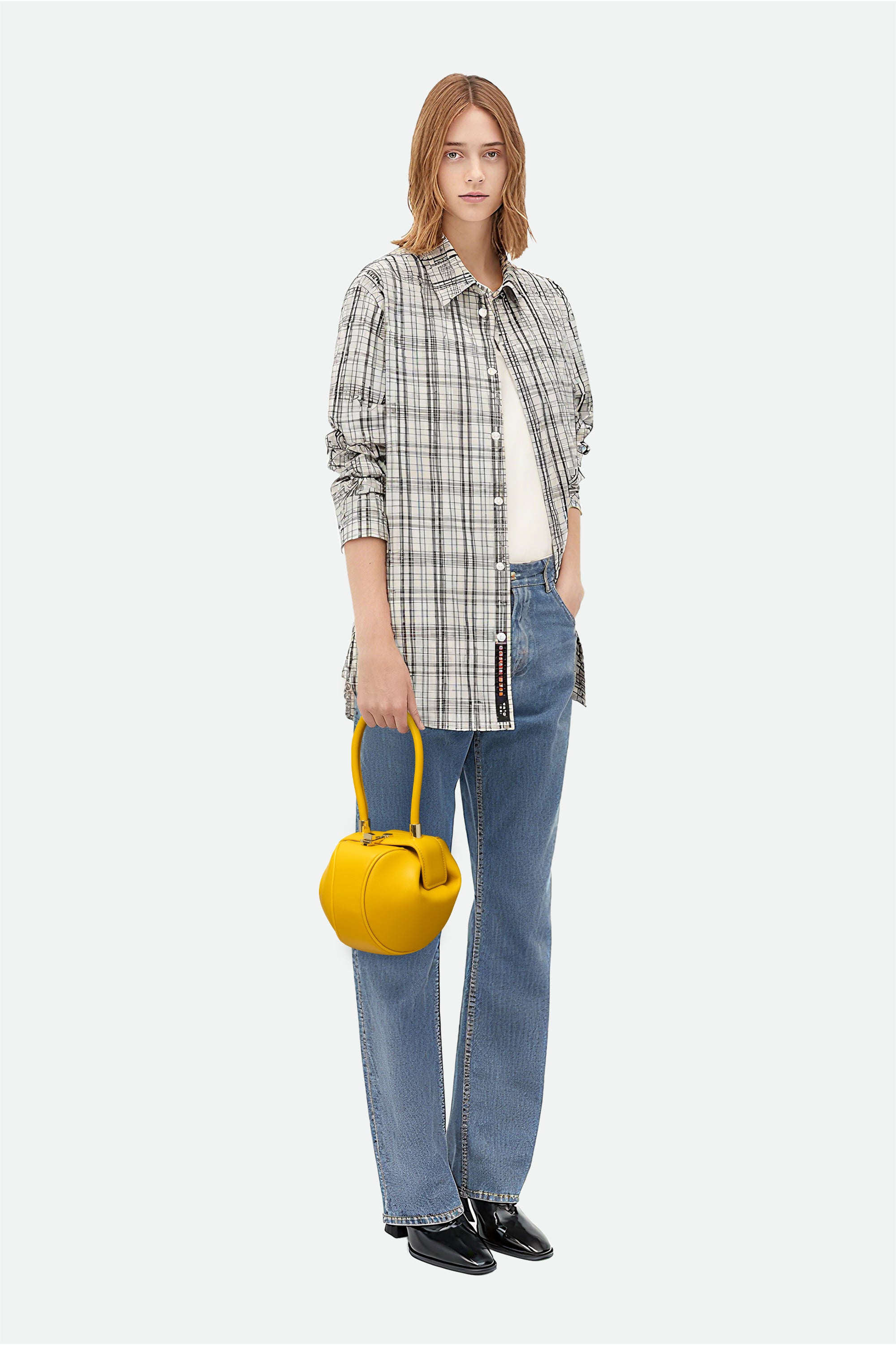 Woman holding a yellow handbag wearing a plaid shirt, jeans, and black shoes on a white background