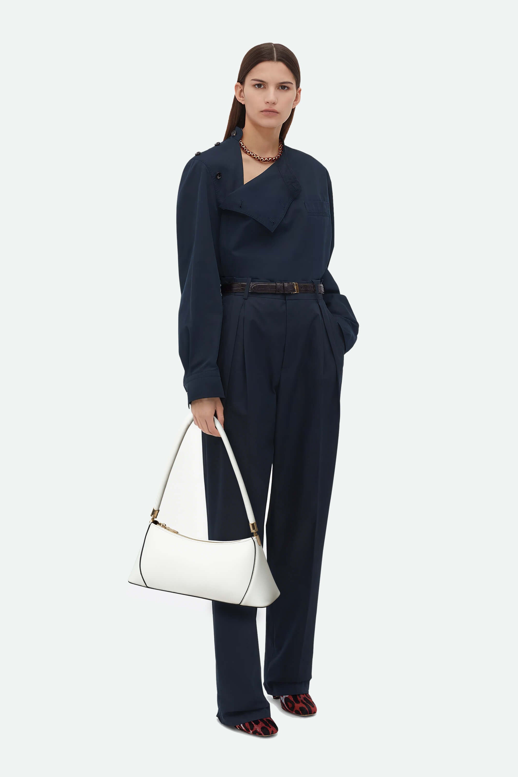 Woman in a navy jumpsuit holding a white handbag on a white background