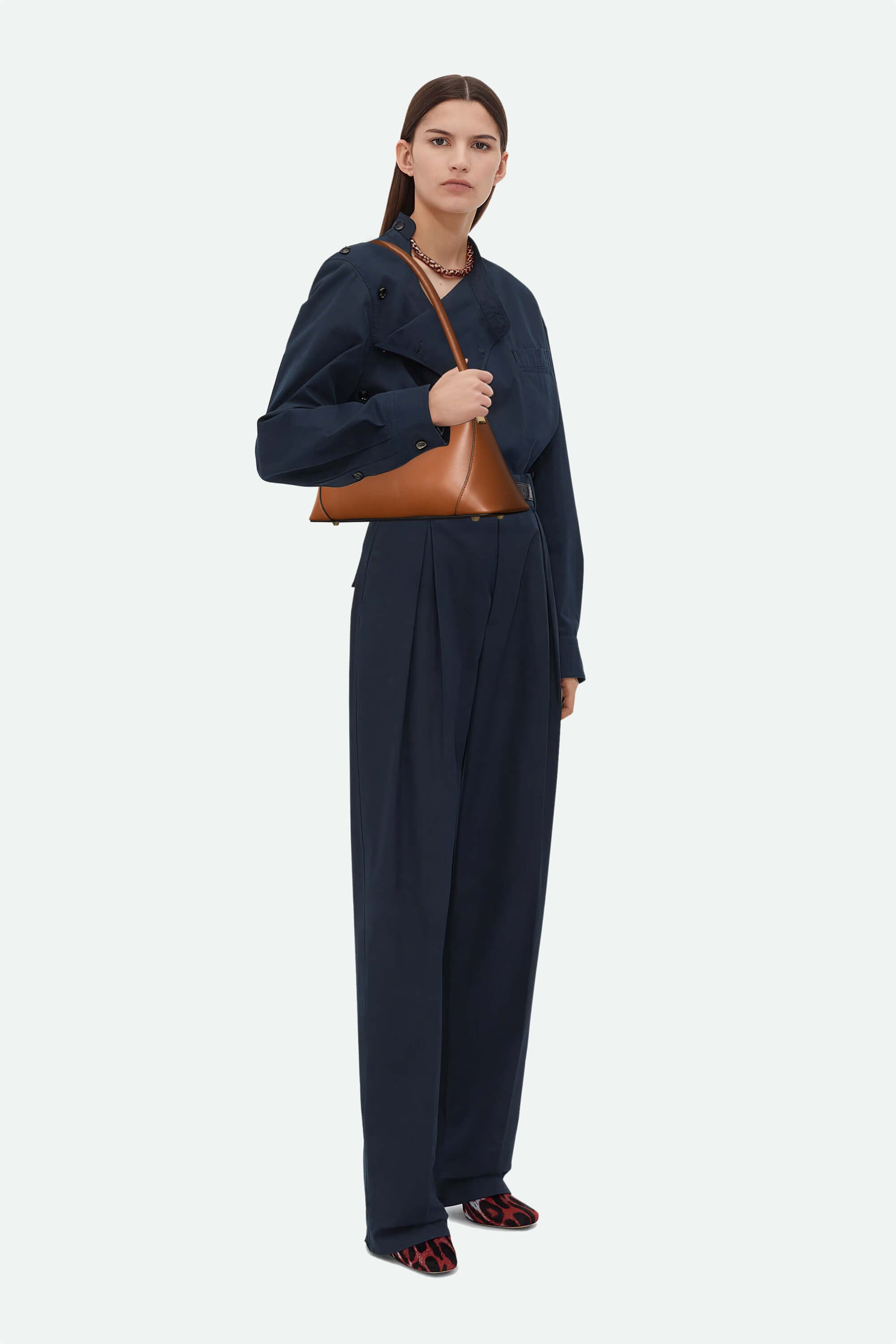 Woman wearing a navy outfit with a brown leather handbag on a white background