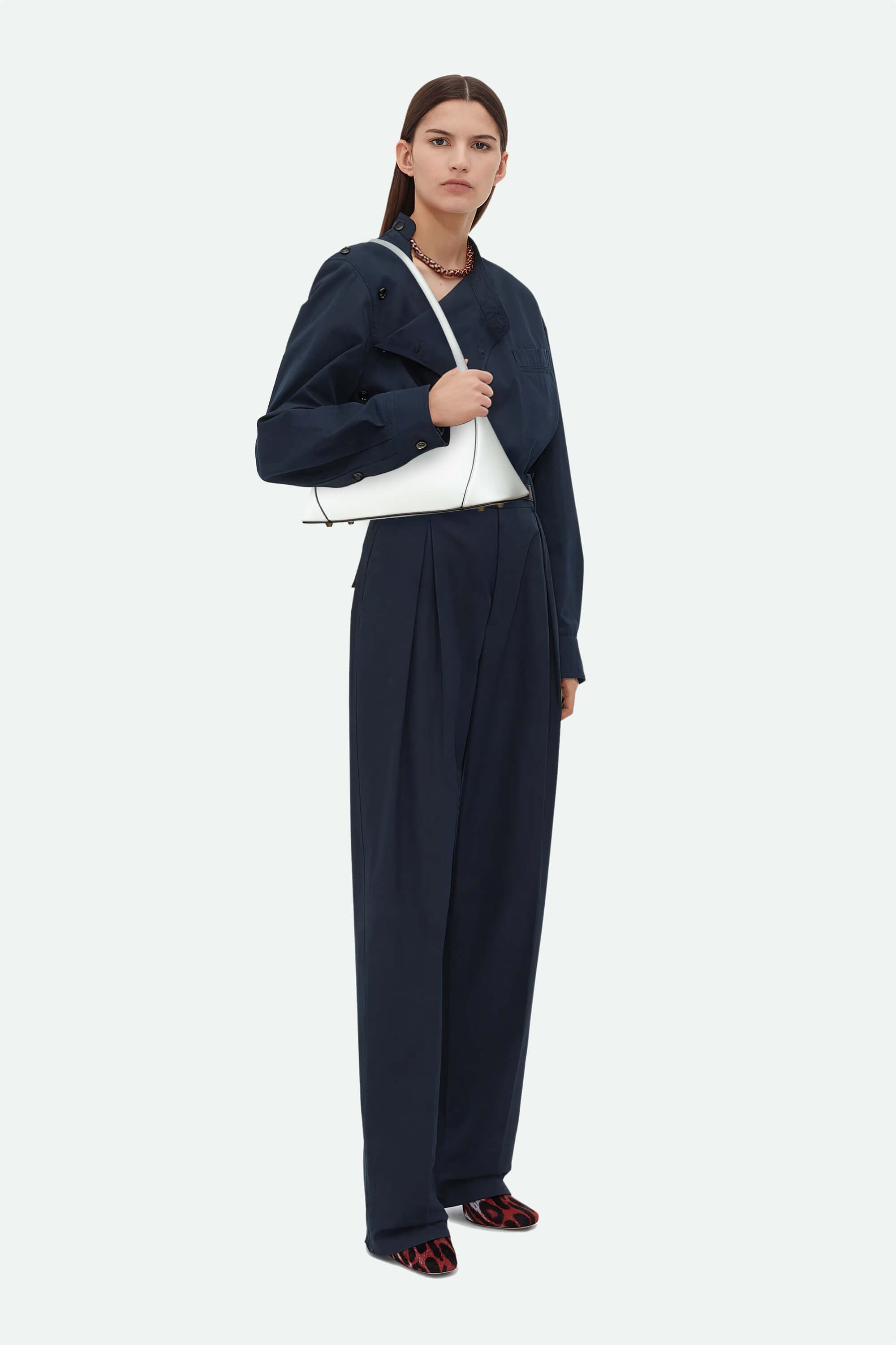 Woman wearing a navy outfit with a white bag on a white background