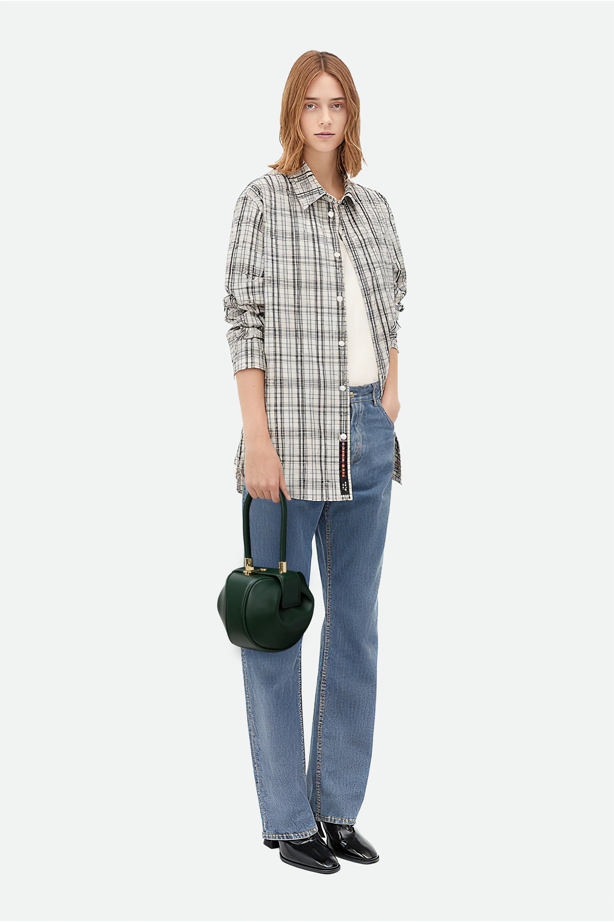 Woman wearing a plaid shirt, jeans, and holding a green handbag on a white background