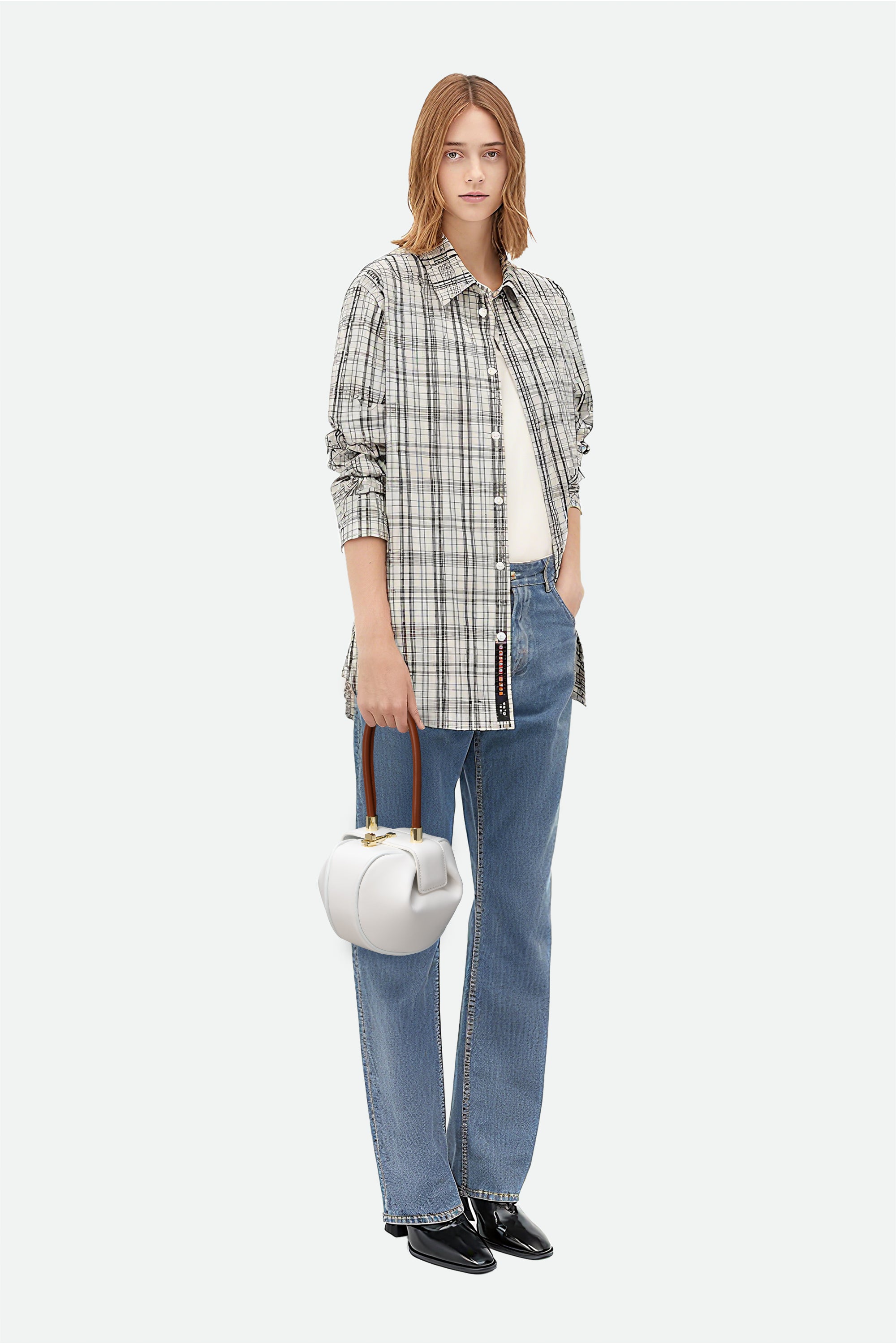 Woman wearing a plaid shirt, jeans, and holding a white handbag on a white background