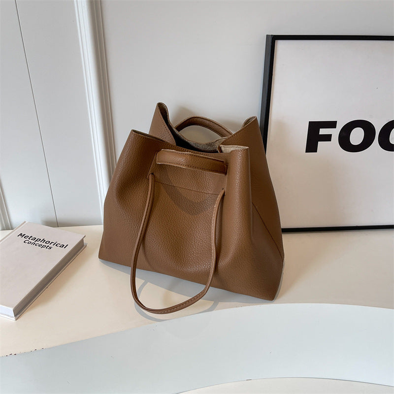 Brown leather tote bag on a white surface with a black frame in the background