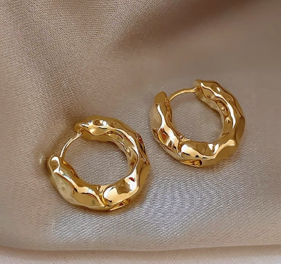 Pair of golden textured hoop earrings on beige satin fabric