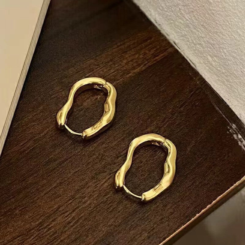 Pair of golden irregular hoop earrings on dark wooden surface