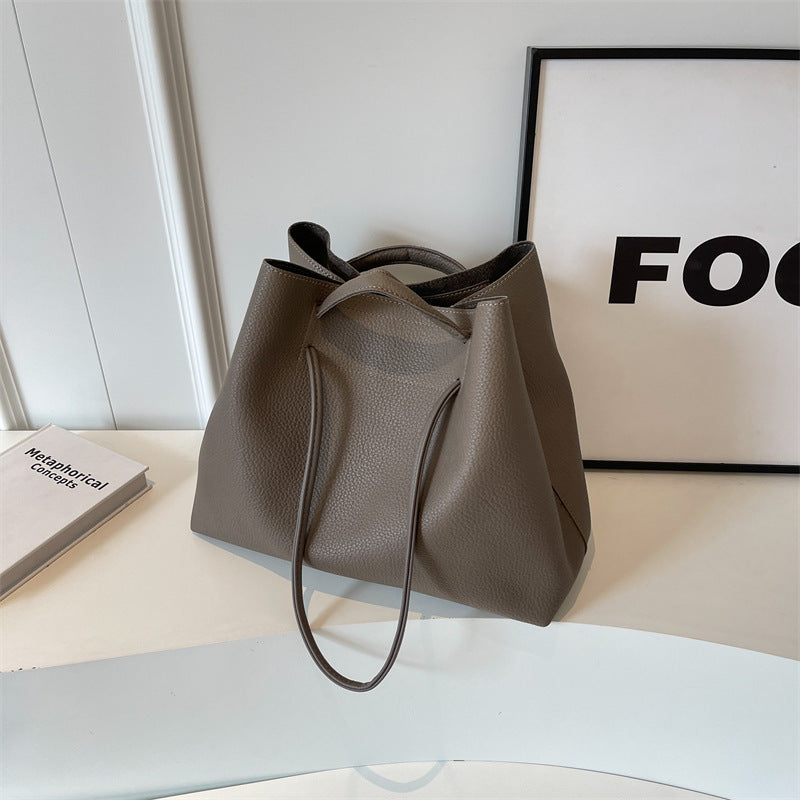 Grey leather tote bag on a white surface with a black frame in the background