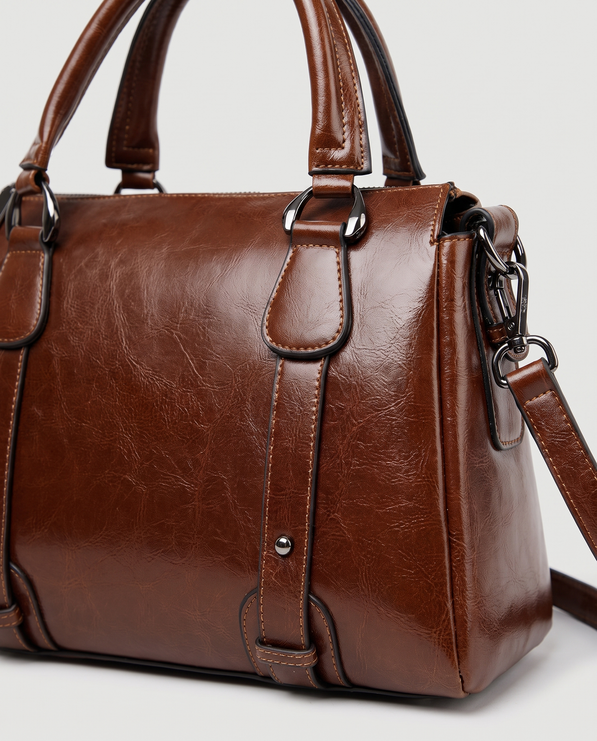 Harlow leather handbag in Coffee – close-up of the top handle, front strap rivets and side ring