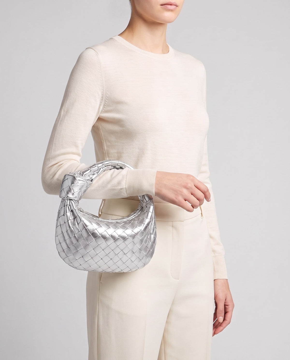 Model carrying the Knot Small woven leather bag in Silver by its knotted handle
