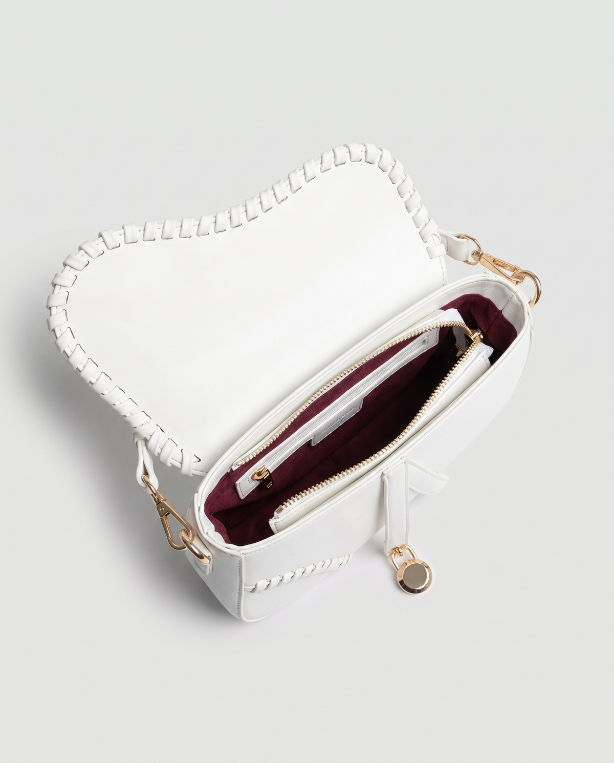 Saddle vegan leather shoulder bag in White – open, showing the burgundy lining and zip pocket