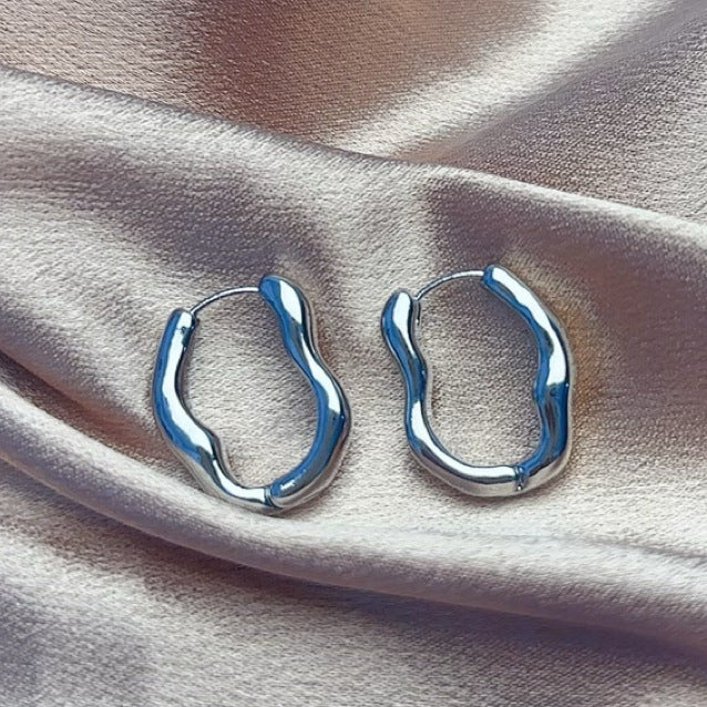 Pair of silver irregular hoop earrings on pink satin fabric