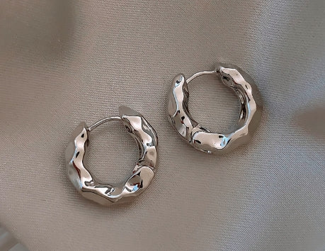 Pair of silver textured hoop earrings on beige satin fabric