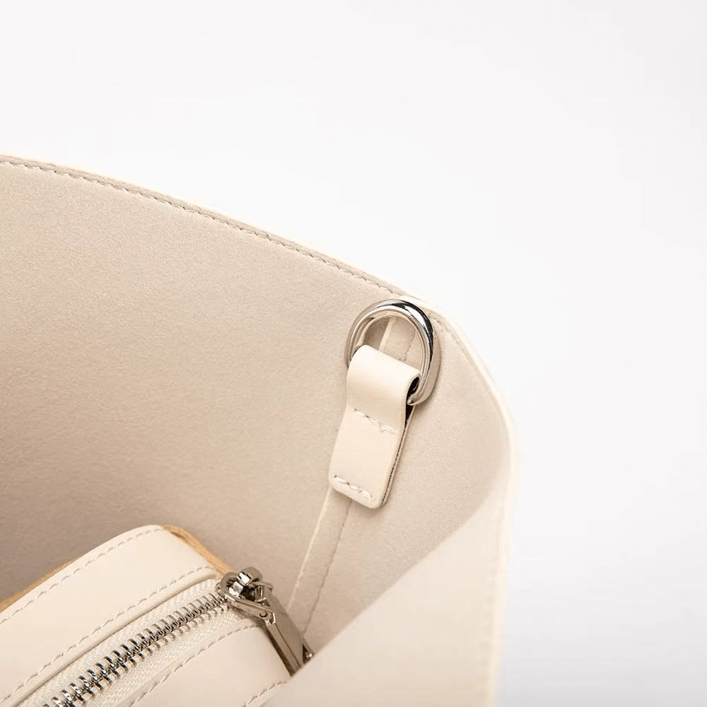 Close-up of a beige handbag with a silver zipper and clasp on a light gray background