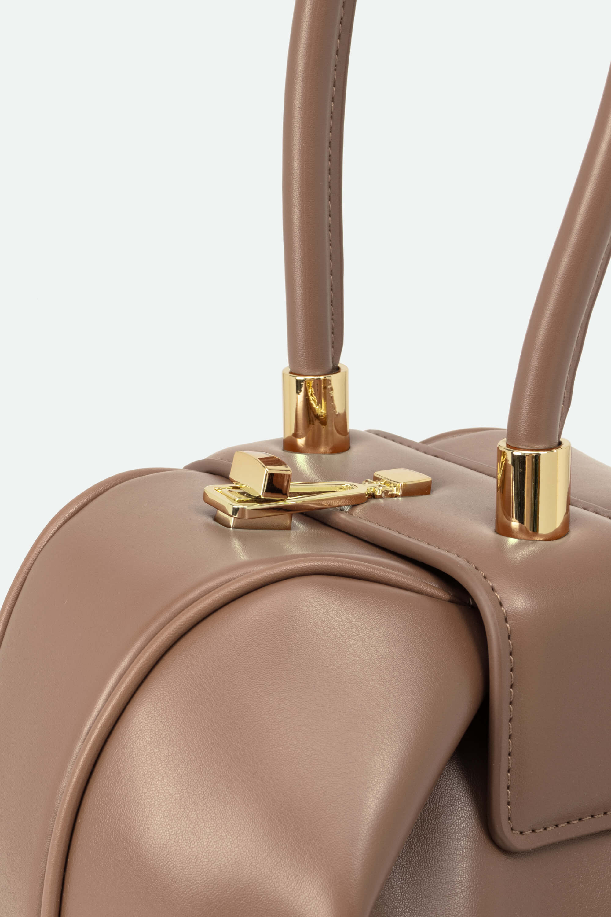 Close-up of a beige handbag with gold handles and clasp on a light gray background