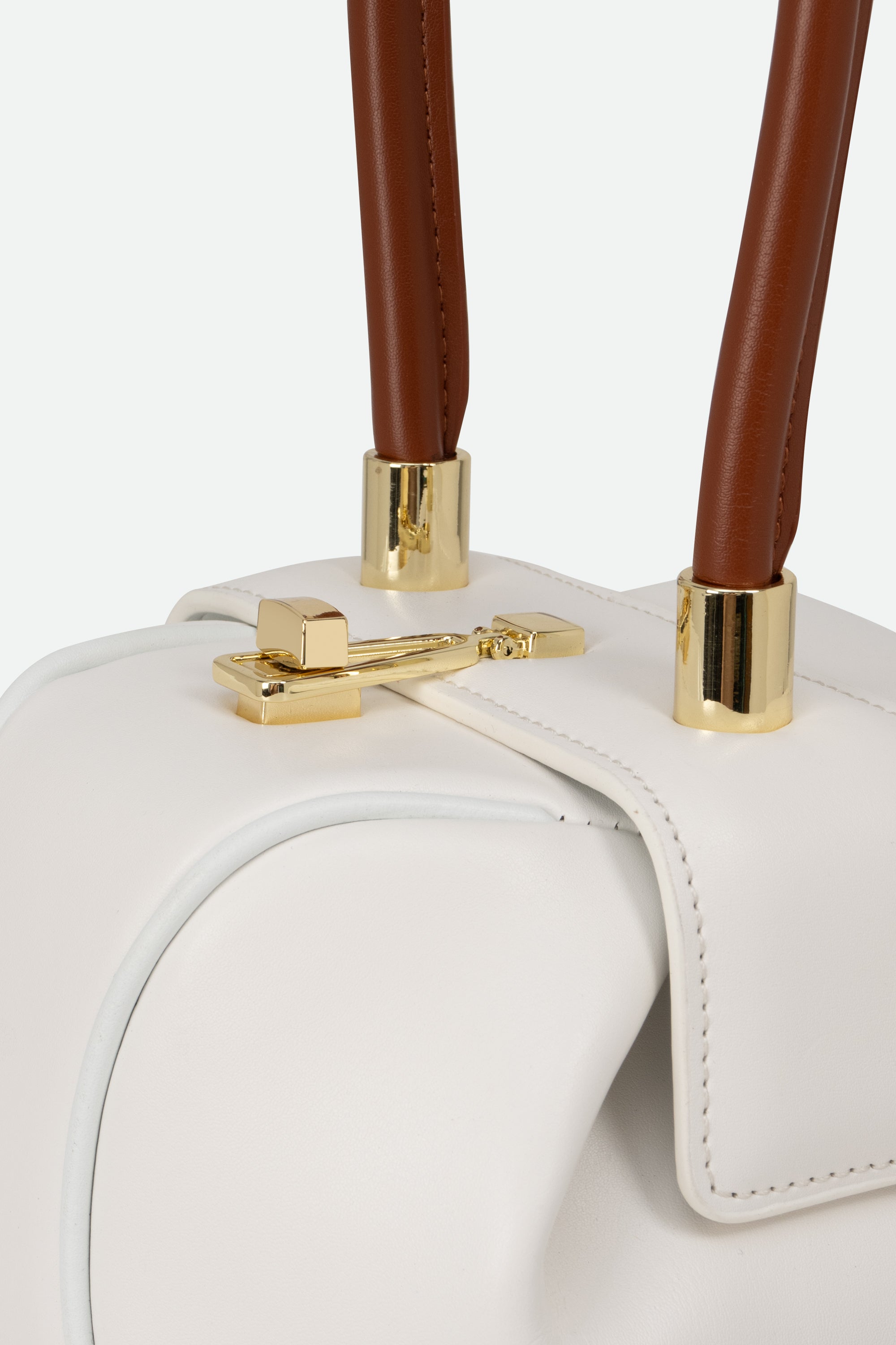Close-up of a white handbag with brown handles and gold hardware on a light gray background