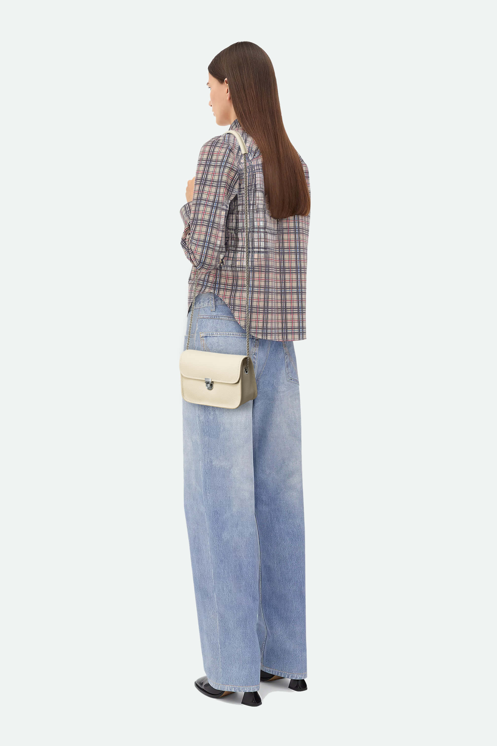 Person wearing a plaid shirt and jeans with a beige handbag on a white background