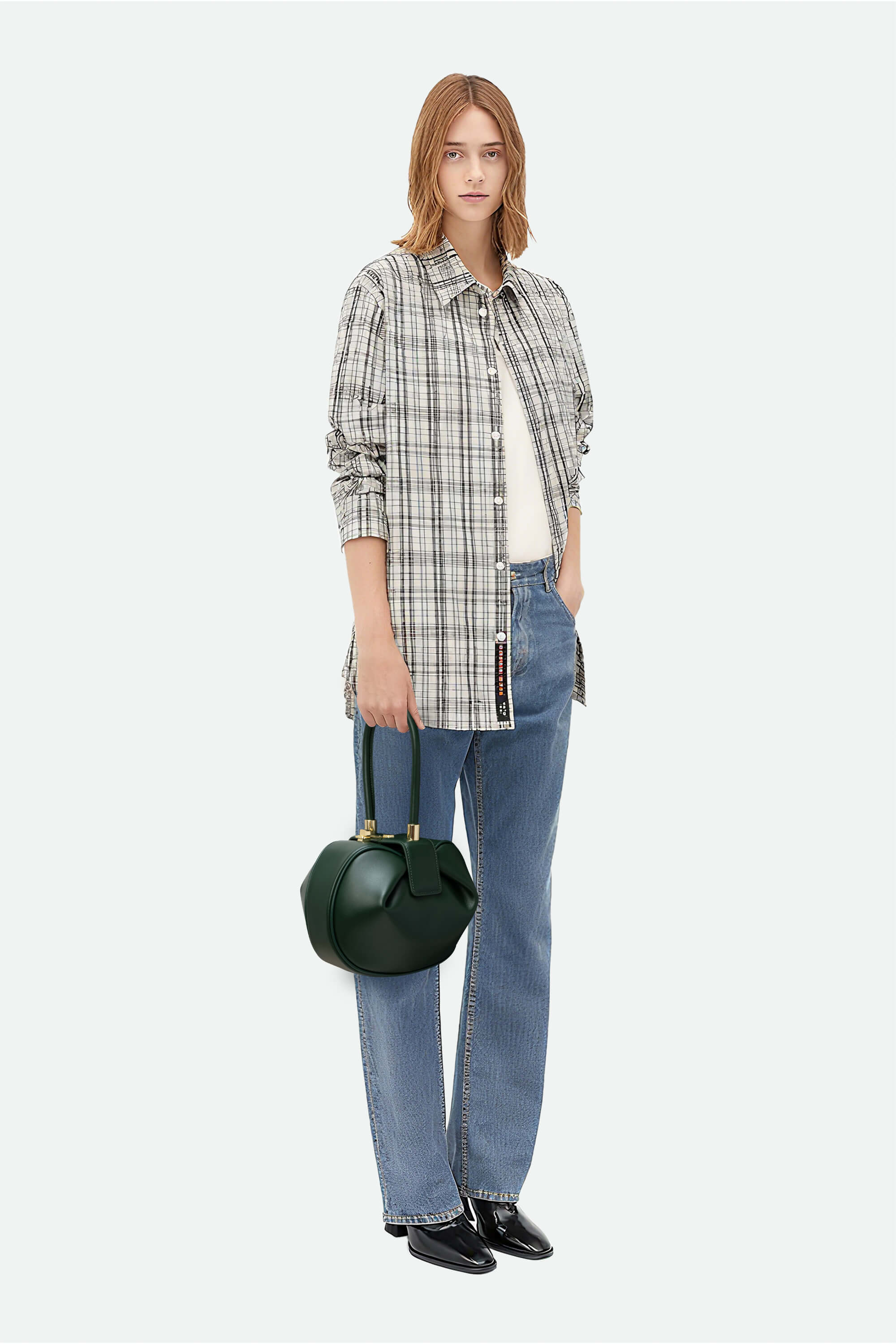 Person wearing a plaid shirt, jeans, and holding a black handbag on a white background