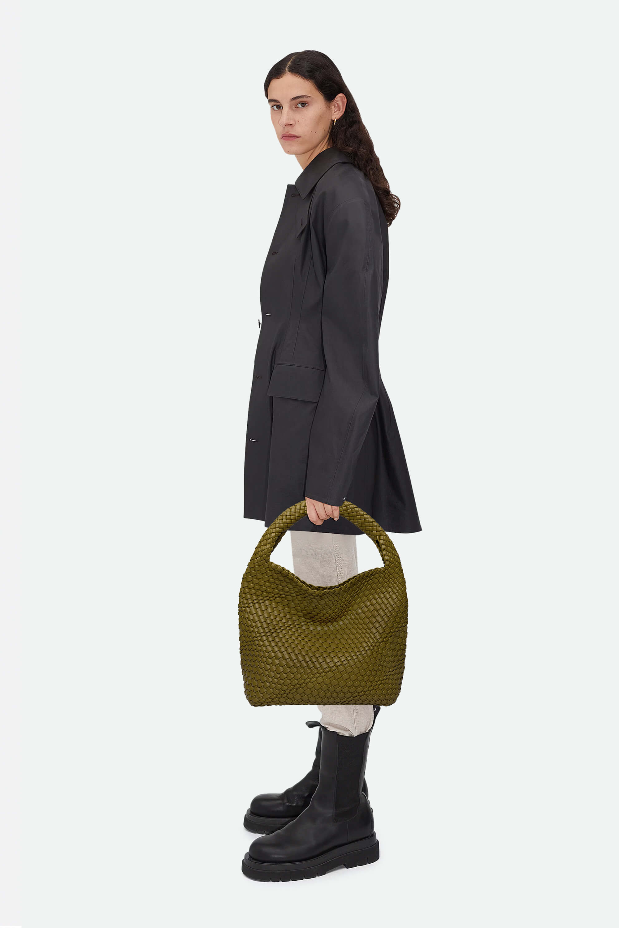 Woman holding a green woven handbag against a white background