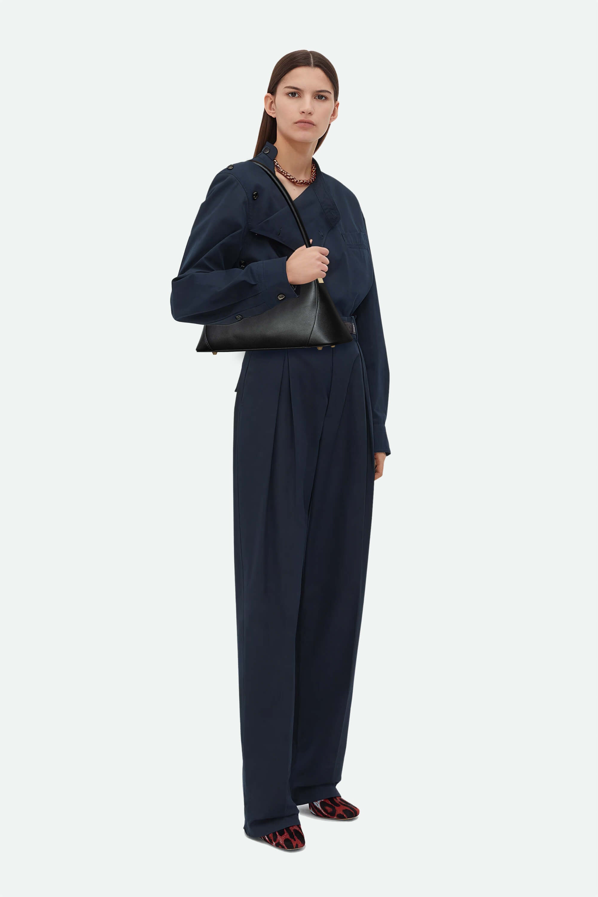 Woman wearing a navy outfit with a black handbag on a white background