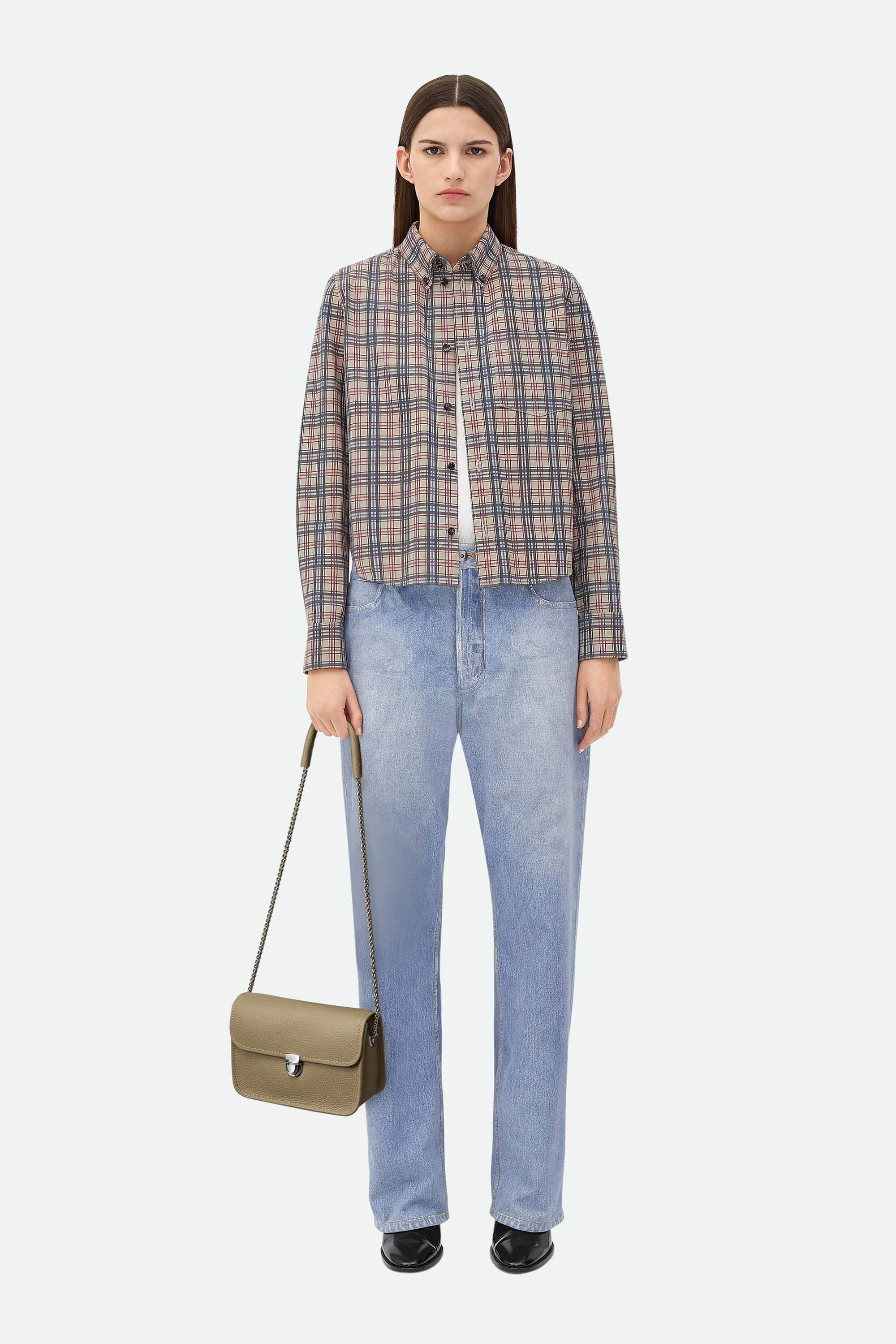 Woman wearing a plaid shirt and blue jeans, holding a green bag on a white background