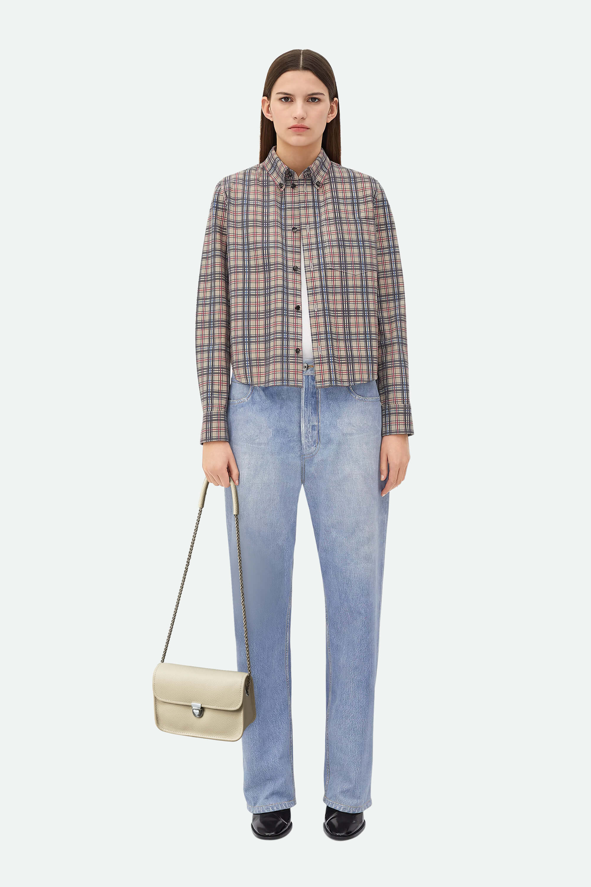 Woman wearing a plaid shirt and jeans with a beige handbag on a white background