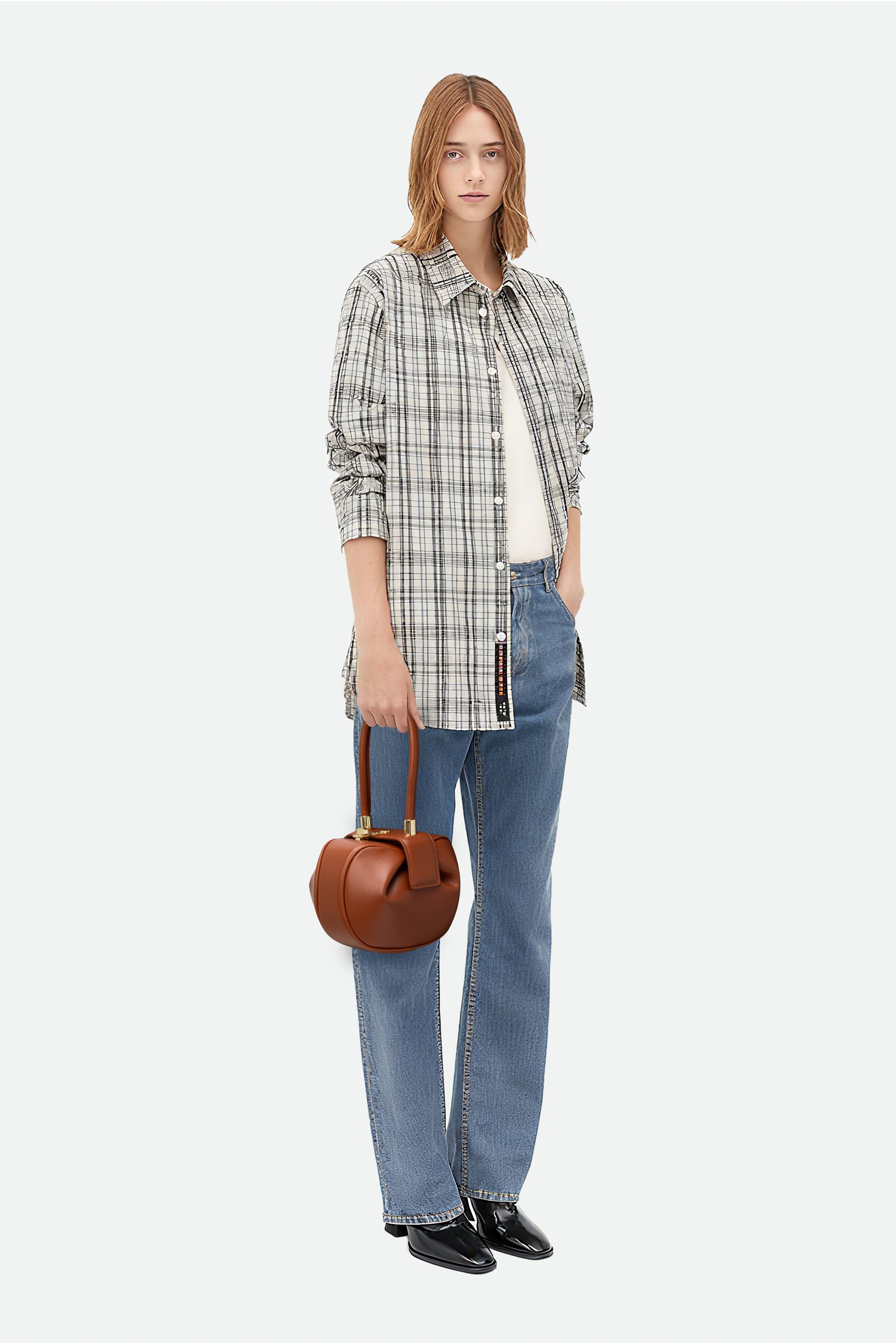 Woman wearing a plaid shirt, jeans, and holding a brown handbag on a white background