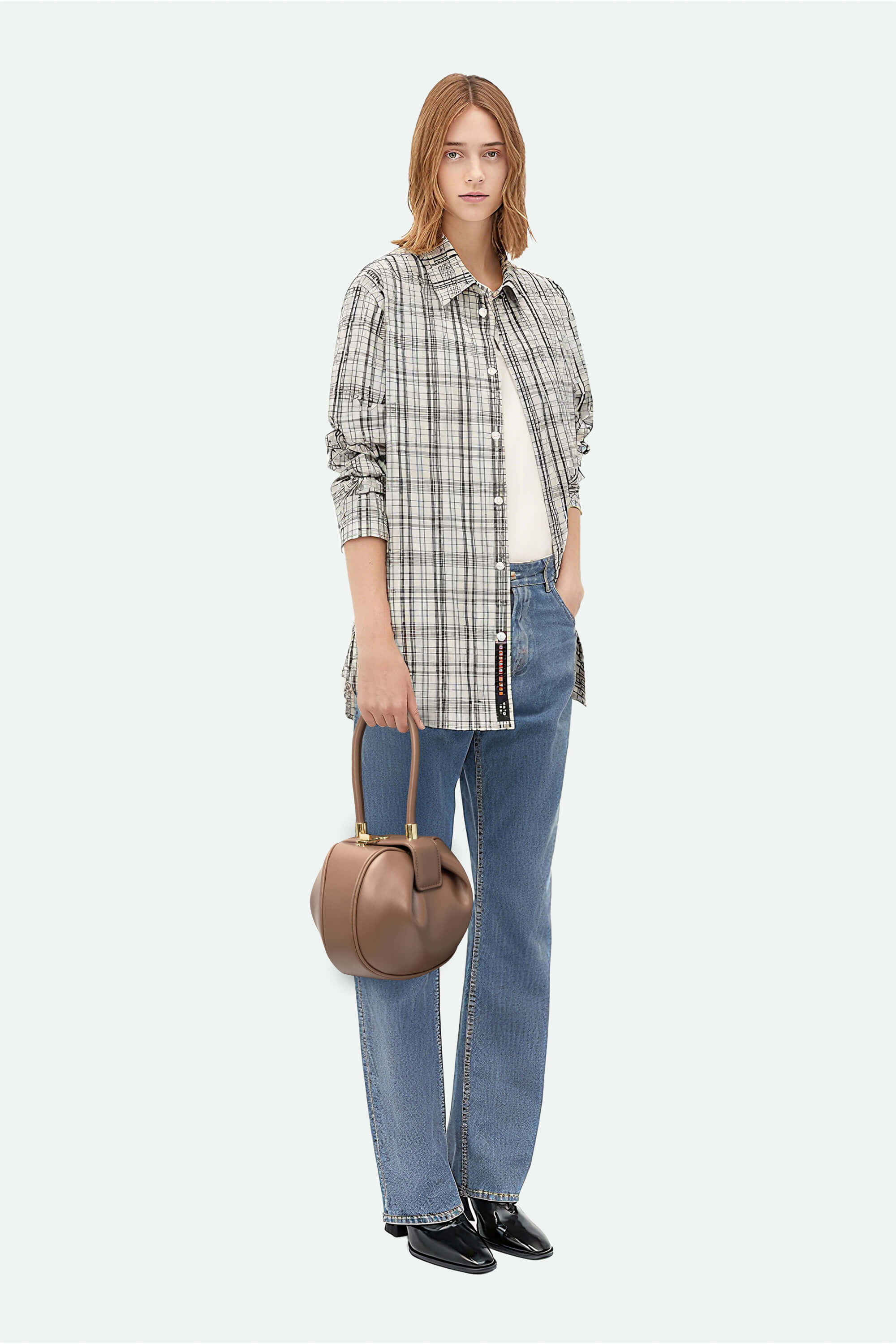 Woman wearing a plaid shirt, jeans, and holding a brown handbag on a white background