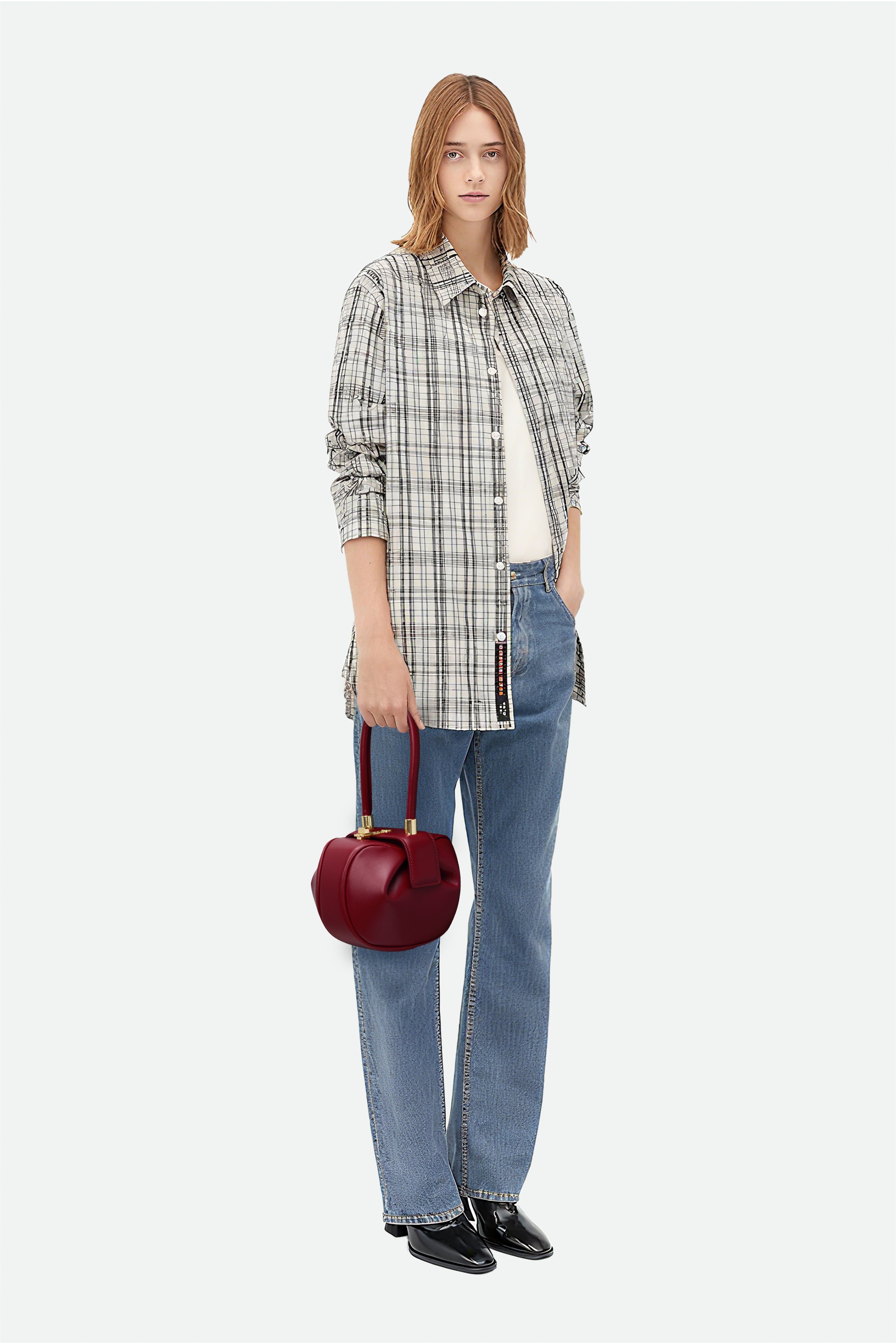 Woman wearing a plaid shirt, jeans, and holding a red handbag on a white background