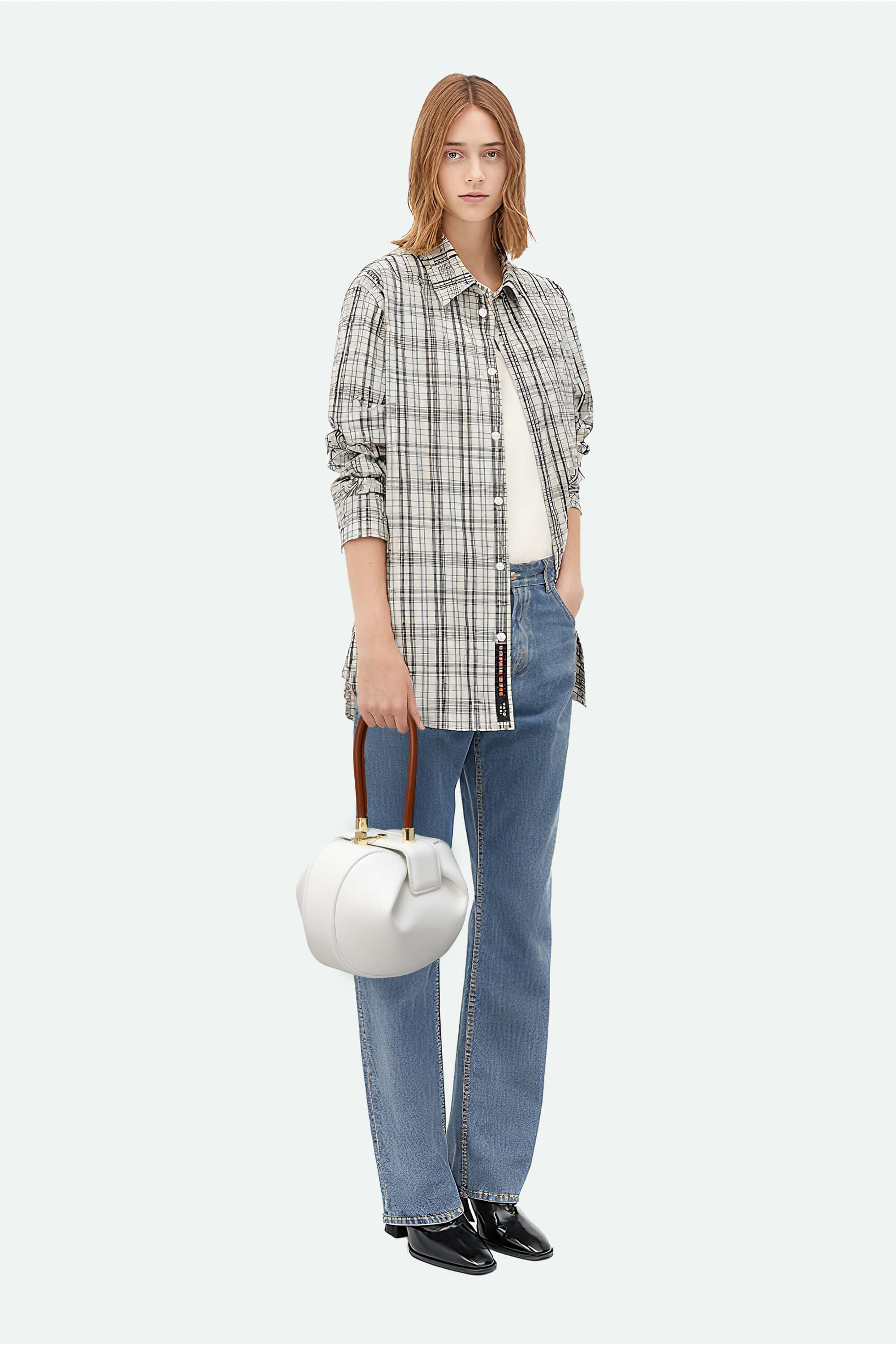 Woman wearing a plaid shirt, jeans, and holding a white handbag on a white background