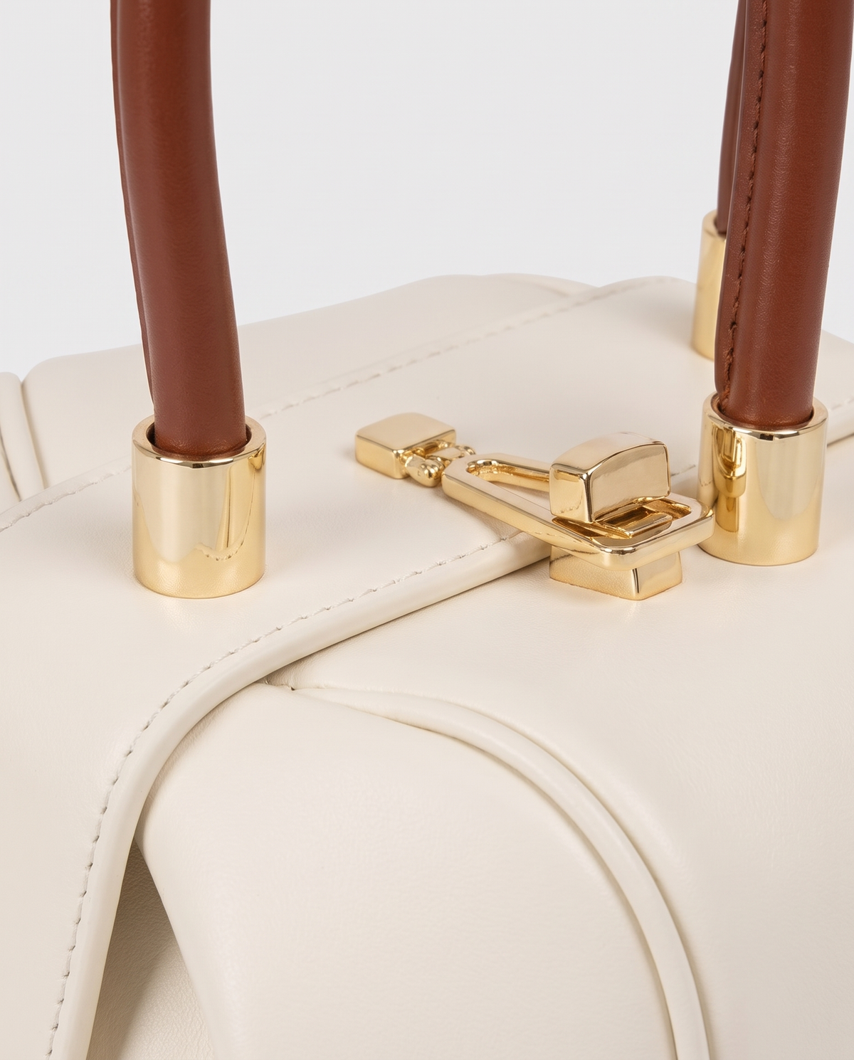 Dumpling Mini leather top-handle bag in White – close-up of the gold twist-lock and handle fittings