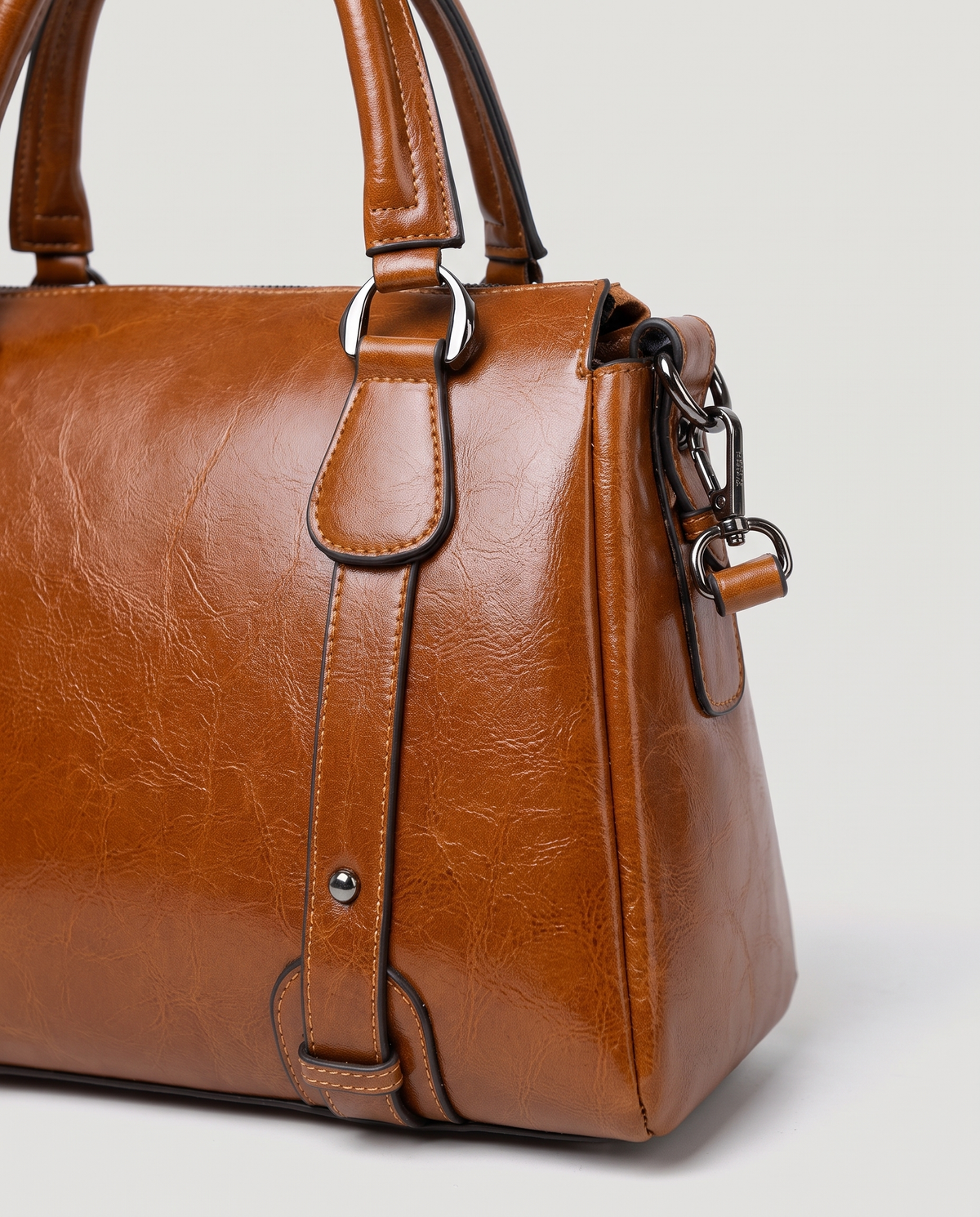 Harlow leather handbag in Brown – close-up of the top handle, front strap rivets and side ring