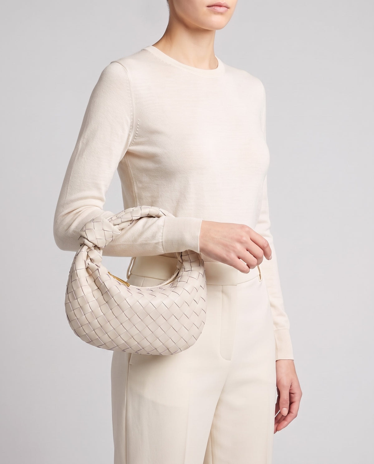 Model carrying the Knot Small woven leather bag in Chalk by its knotted handle