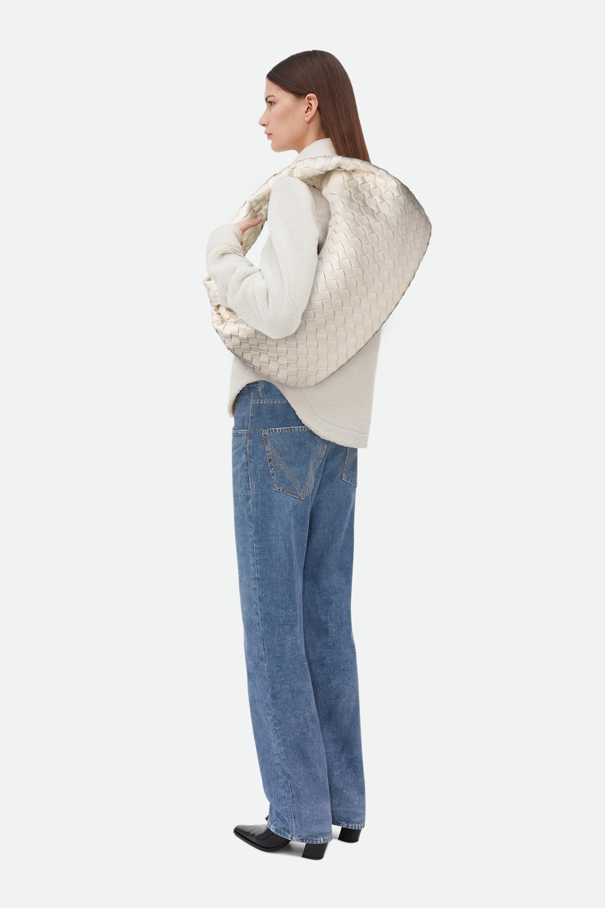 Woman carrying Large Knot Bag (Jodie) while wearing a beige quilted jacket, white sweater and blue jeans on a white background