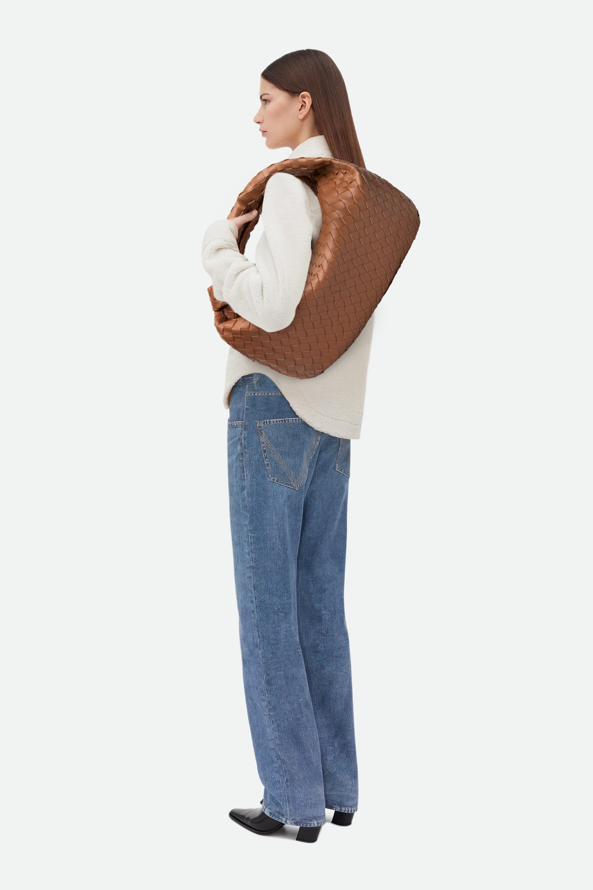 Woman wearing a white sweater and blue jeans carrying Large Knot Bag (Jodie) brown woven handbag on her shoulder