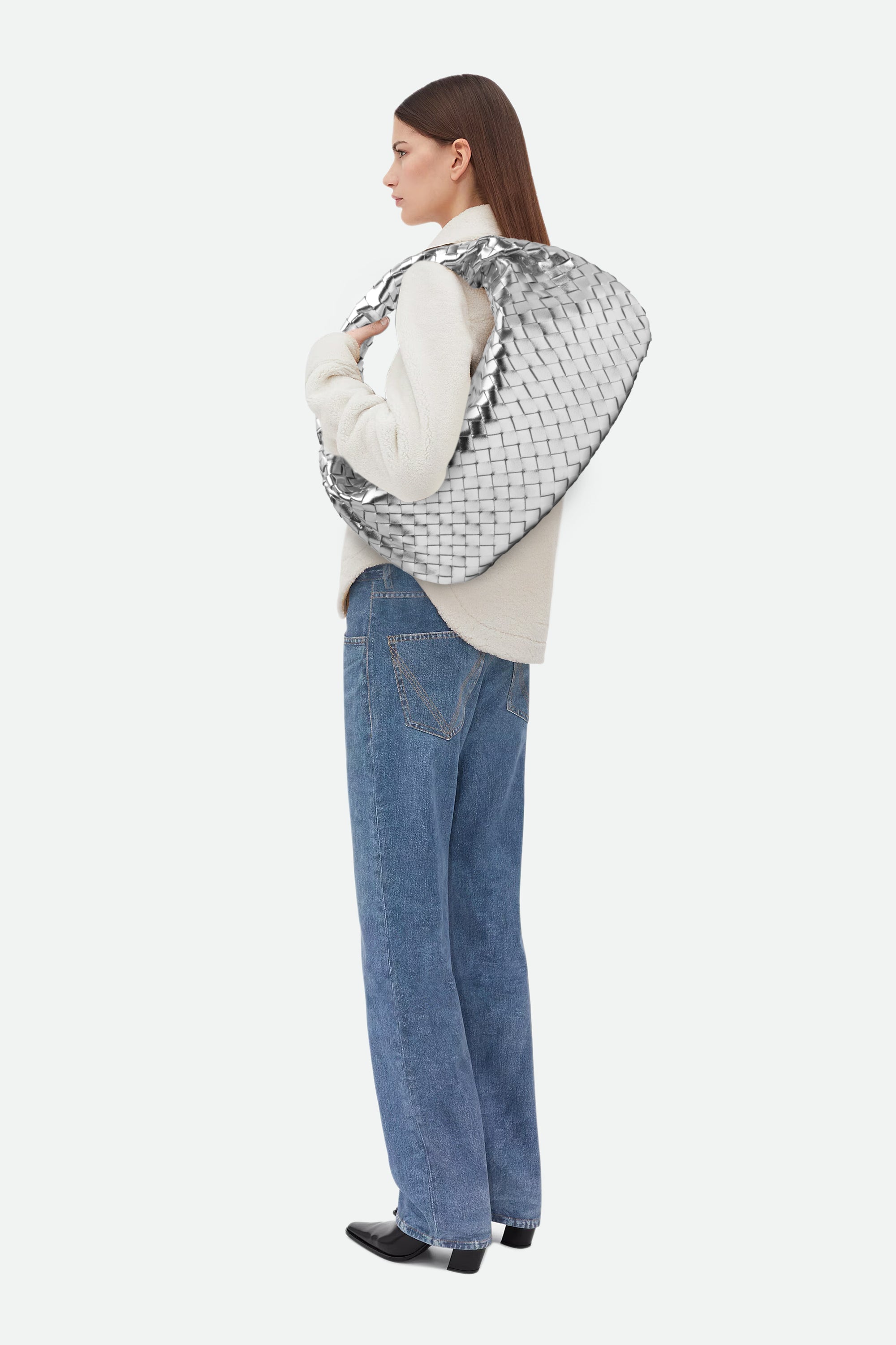 Woman wearing a light sweater and blue jeans carrying Large Knot Bag (Jodie) silver woven handbag on her shoulder.