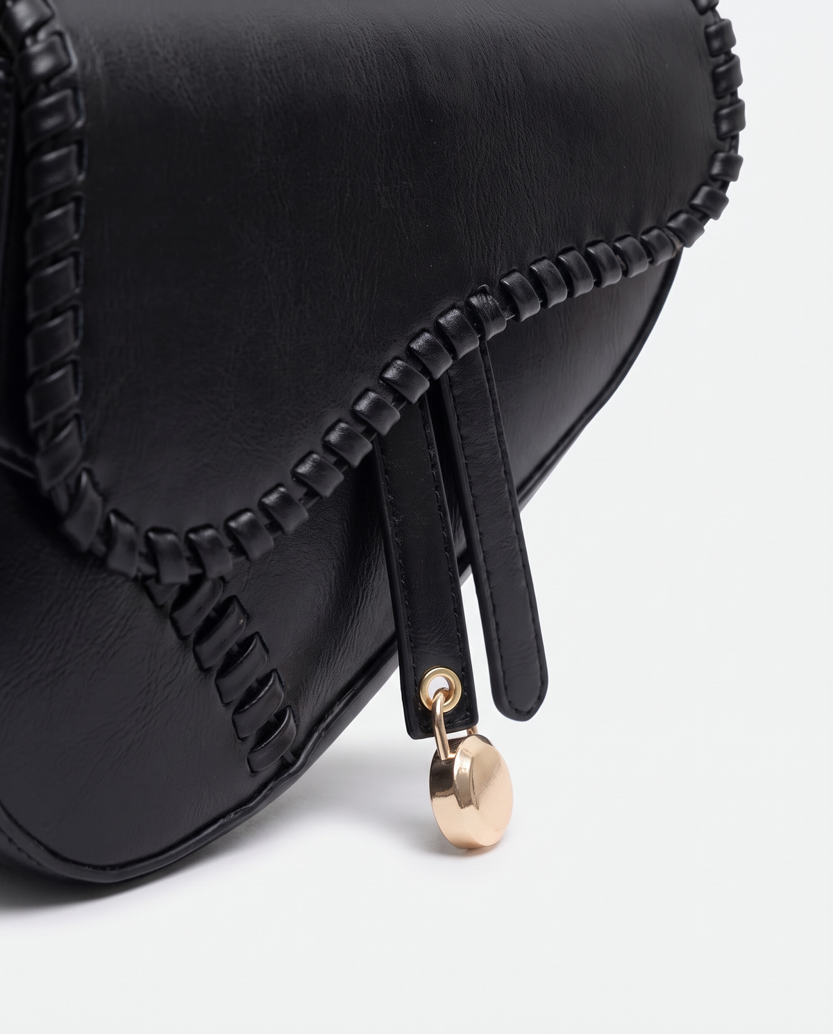 Saddle vegan leather shoulder bag in Black – close-up of the whipstitched edge and gold padlock charm