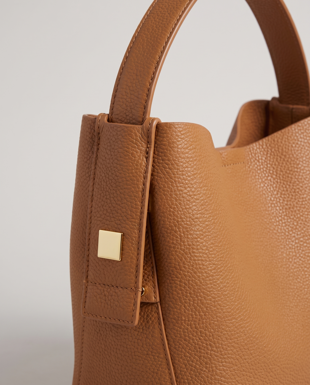 Transit leather bucket bag in Caramel – close-up of the handle tab and gold hardware